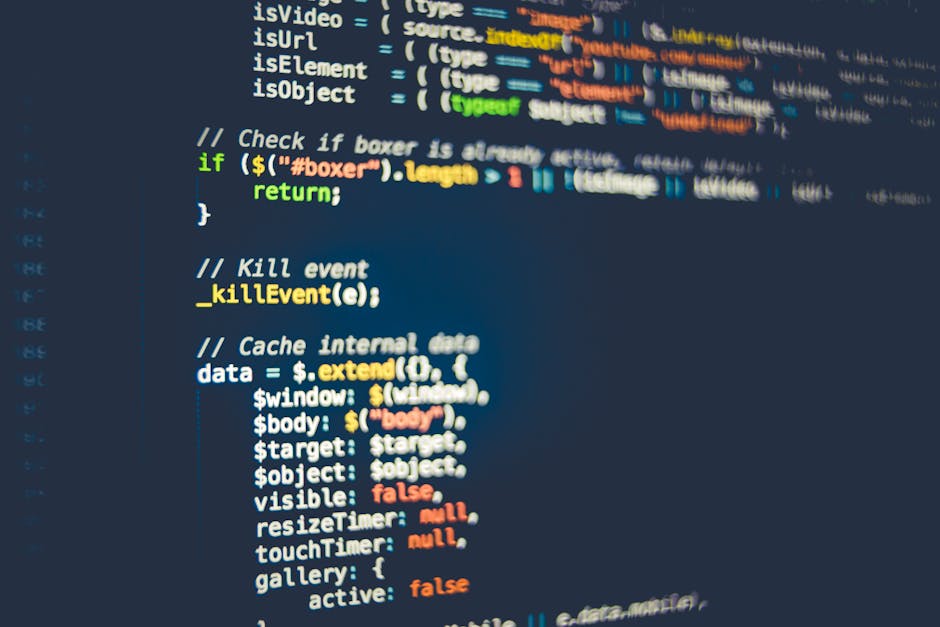 A close-up view of a laptop screen displaying a programming code editor with lines of coded text in various colors, including blue, green, and black, set against a dark background. The screen emits a 